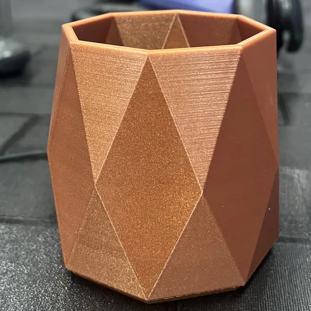 The 3D-printed faceted pen holder in copper-coloured filament, photographed on a desk.